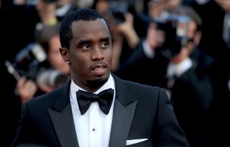 A man in a tuxedo poses at a red carpet event with cameras in the background.