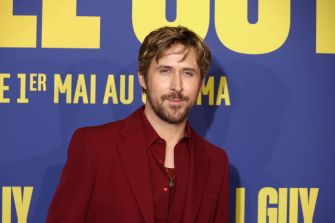 Ryan Gosling at a promotional event, wearing a red outfit against a colorful backdrop.