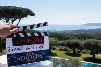 Clapperboard for The White Lotus Season Four on a scenic film set overlooking a coastal landscape.