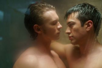 Two shirtless male characters face each other intimately in a steamy setting.