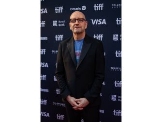 Photograph of filmmaker Steven Soderbergh at the Toronto International Film Festival, wearing a black suit and standing in front of a sponsor backdrop.