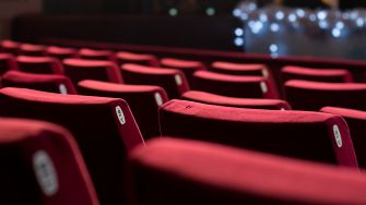 Empty red theater seats with dim lighting in the background.
