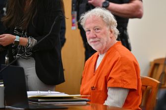 Timothy Busfield appearing in court wearing an orange jumpsuit, with law enforcement officers present in the background.