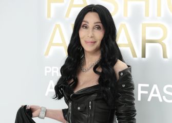 Image of Cher at an award event, wearing a black outfit and smiling at the camera.