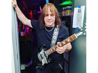 Ross "the Boss" Friedman holding a guitar, posing at a venue.