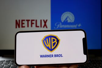 A smartphone displaying the Warner Bros. logo, with Netflix and Paramount+ logos blurred in the background.