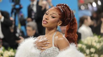 Megan Thee Stallion wearing a sparkling outfit and posing confidently at a public event, surrounded by a blurred audience.