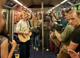 Ed Sheeran performing on the subway while surrounded by fans and a film crew for the Netflix special "One Shot With Ed Sheeran."