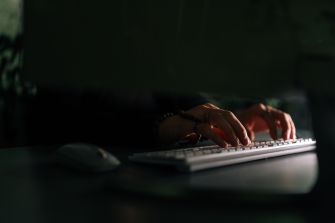 A close-up of hands typing on a keyboard in a dimly lit environment.