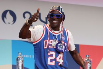 Flavor Flav giving a thumbs up while wearing Team USA gear, showcasing his enthusiasm for the Olympics.