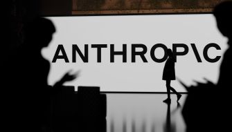 A silhouette of a person walking in front of a large display featuring the word "ANTHROPIC."