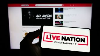 A person holding a smartphone displaying the Live Nation Entertainment logo, with a blurred screen showing video content in the background.