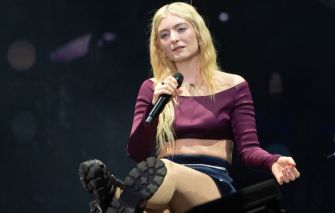 Lorde performing on stage with a microphone during a live concert.