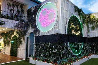 Exterior of Casa Amor, a location featured in the reality show Love Island, showcasing vibrant neon signage and lush greenery.