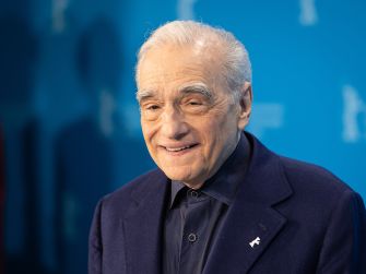 Martin Scorsese at an event, smiling and wearing a dark suit against a blue backdrop.
