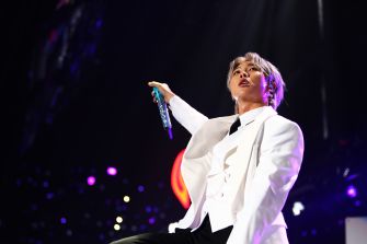 RM performing on stage, despite an ankle injury, wearing a white suit and holding a microphone.