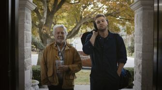 A scene featuring two men standing at a doorway, one older and one younger, during autumn.