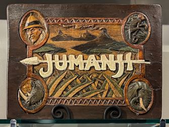 Carved wooden display featuring the word "Jumanji" along with intricate animal and character motifs.