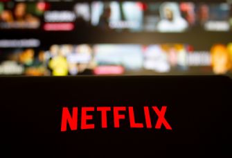 Close-up of a Netflix logo displayed on a device with a blurred background of streaming content.