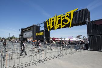 Entrance gate of Hellfest festival, with attendees lined up and signs showing extreme heatwave conditions.